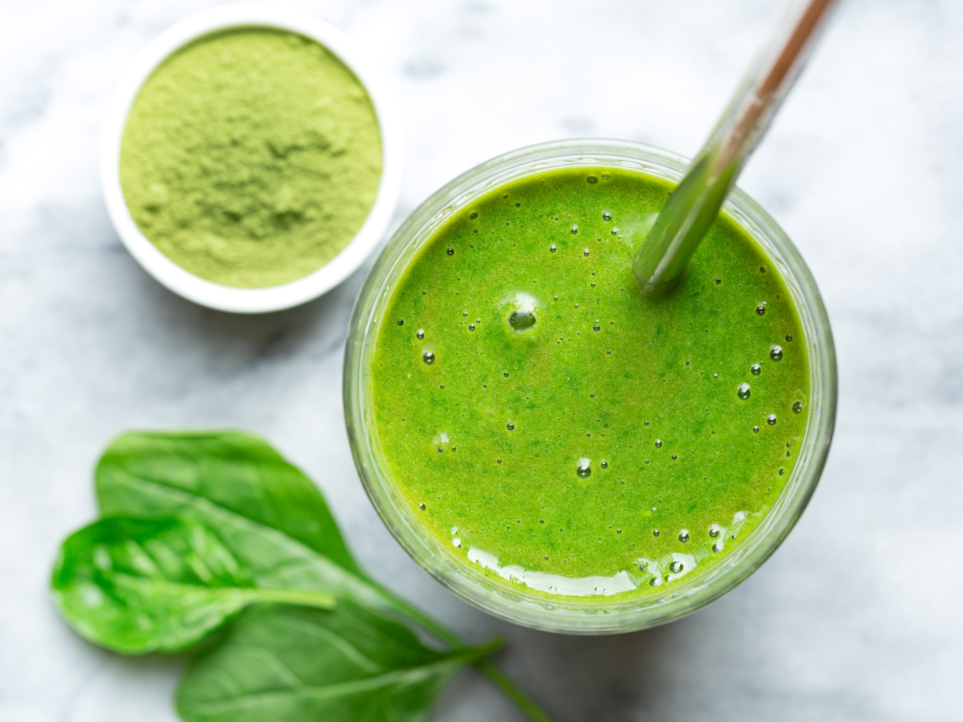 a green smoothie with spinach leaves and green powder on the table